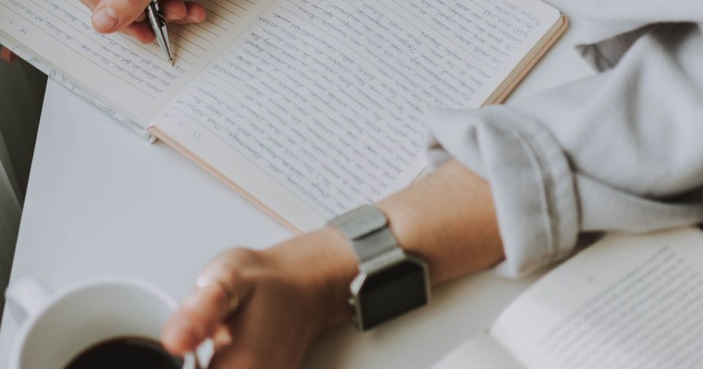 Person writing in a journal beside a cup of coffee