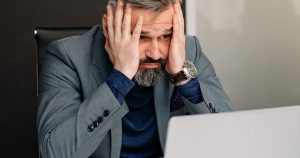 Frustrated person with hands on face looking at a slow laptop