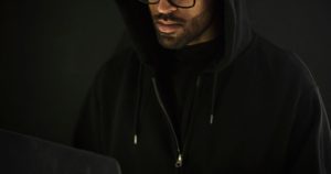 Person in a hoodie using a laptop in a dark room